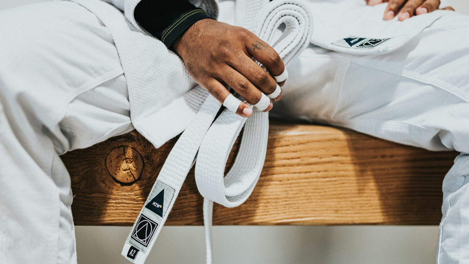 Person wearing a white martial arts uniform with a white belt on a wooden bench.